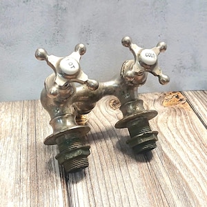 May include: Antique silver-toned faucet with cross-shaped handles. The faucet has "HOT" and "COLD" labels on the white handle inserts. The faucet is mounted on a wooden surface.