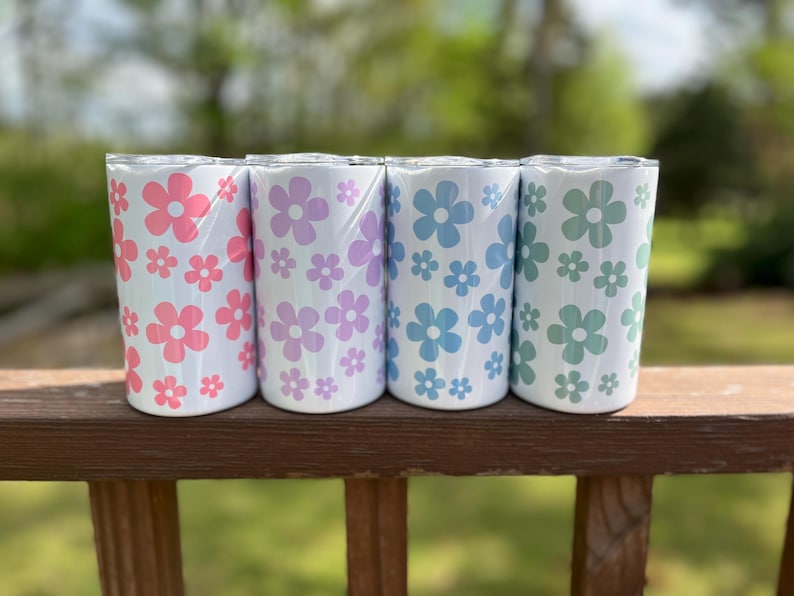 May include: Four stainless steel tumblers with a white background and a pattern of pink, purple, blue, and green flowers.