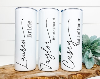 May include: Three white stainless steel tumblers with black calligraphy. The tumblers are labeled "Lauren Bride", "Taylor Bridesmaid", and "Casey Maid of Honor".