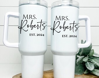 May include: Two white travel mugs with black handles and lids. The mugs are personalized with the text "MRS. Roberts EST. 2024".