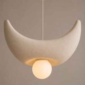 Op de afbeelding: Een halvemaanvormige hanglamp met een getextureerde, gebroken witte matte afwerking. De lamp hangt aan een dunne stang aan een ronde plafondkap en is voorzien van een enkele, gloeiende bolvormige glazen lamp aan de onderzijde.