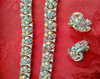 Op de afbeelding: Een set met iriserende strass-sieraden met een paar clip-on oorbellen en een armband. De sieraden zijn zilverkleurig en hebben een bloemmotief.