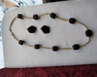 May include: A gold chain necklace with black faceted beads and matching black faceted earrings. The necklace is on a white surface.