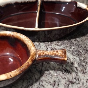 May include: A set of two brown and white glazed ceramic serving dishes. The larger dish is oval shaped and divided into two sections. The smaller dish is round with a handle.