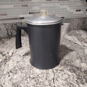 May include: A black metal coffee pot with a silver lid and a black handle. The pot is sitting on a granite countertop.