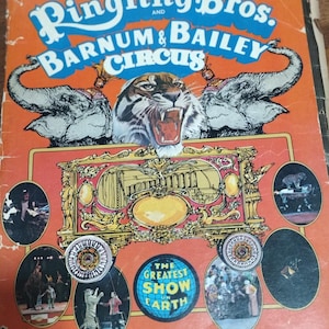 May include: A vintage program from the 100th anniversary of Ringling Bros. and Barnum & Bailey Circus. The cover features a tiger roaring with elephants in the background. The program includes photos of various circus acts, including a tiger, clowns, and a trapeze artist. The text "The Greatest Show on Earth" is featured on the cover.