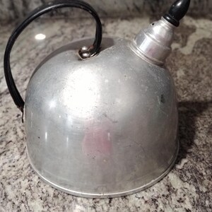 May include: A silver aluminum tea kettle with a black handle and a black knob on the lid.