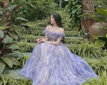 May include: A light purple off-the-shoulder gown with a floral pattern. The dress features a layered skirt and is worn outdoors among lush greenery. The image includes the text "MV305" in the lower left corner.