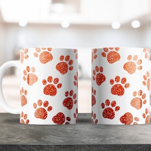 May include: Two white ceramic mugs with a red paw print pattern. The mugs have a white interior and a white handle.