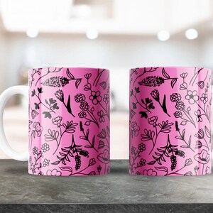 May include: Two ceramic mugs with white handles and a pink background. The mugs feature a black floral pattern of various flowers and leaves. The mugs are displayed on a dark gray surface.