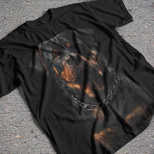 Puede incluir: Camiseta negra con una imagen de primer plano de un perro Rottweiler con un collar de cadena de plata.