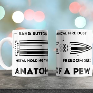 May include: White ceramic mug with a black illustration of the anatomy of a gun. The text on the mug reads "BANG BUTTON", "MAGICAL FIRE DUST", "METAL HOLDING THING", "FREEDOM SEED", and "ANATOMY OF A PEW".