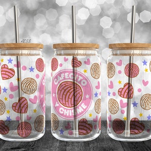 Puede incluir: Tres vasos de vidrio transparente con diseños de patrones rosas y marrones. Los vasos tienen tapas de madera y pajitas de metal. El vaso del medio tiene el texto "Cafecito y Chismes" en un círculo rosa.