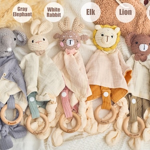 K&ouml;nnte beinhalten: F&uuml;nf geh&auml;kelte Babyspielzeuge mit angeh&auml;ngten Musselin-Decken und Holz-Bei&szlig;ringen. Die Spielzeuge sind ein grauer Elefant, ein wei&szlig;es Kaninchen, ein brauner Elch, ein gelber L&ouml;we und ein brauner B&auml;r. Die Ringe sind mit den Namen "Yanni", "Opaline", "Tummy", "Baby EJ" und "Little Dreamer" graviert.