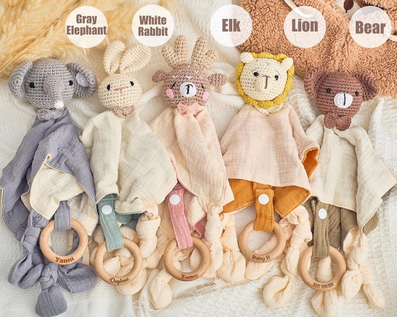 K&ouml;nnte beinhalten: F&uuml;nf geh&auml;kelte Babyspielzeuge mit angeh&auml;ngten Musselin-Decken und Holz-Bei&szlig;ringen. Die Spielzeuge sind ein grauer Elefant, ein wei&szlig;es Kaninchen, ein brauner Elch, ein gelber L&ouml;we und ein brauner B&auml;r. Die Ringe sind mit den Namen "Yanni", "Opaline", "Tummy", "Baby EJ" und "Little Dreamer" graviert.