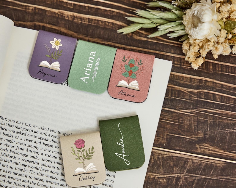 May include: Five magnetic bookmarks in purple, light green, pink, beige, and dark green. Each features a printed illustration of a flower emerging from an open book and a name: Beyonca, Ariana, Athena, Oakley, and Amelia, with decorative leaf accents.