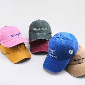 May include: Four different baseball caps with various embroidered designs. The caps are in pink, blue, green, and brown. The designs include "Your Logo", "Your Text", "Happy Wife Happy Life", and "Grumpy".