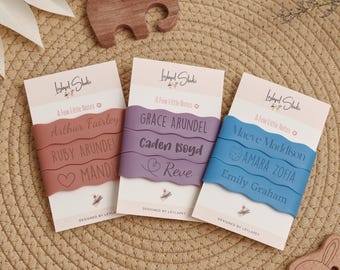 May include: Three sets of wavy silicone bands in terracotta, purple, and blue, each wrapped around a white card labeled Leylapet Studio and A Few Little Notes. The bands are engraved with various names including Arthur Fairley, Grace Arundel, and Maeve Maddison, along with small heart and fox icons.