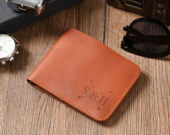 May include: A brown leather wallet with the initials "S & H" and arrows engraved on the front. The wallet is rectangular and appears to be new. The stitching is visible around the edges. The wallet is on a wooden surface.