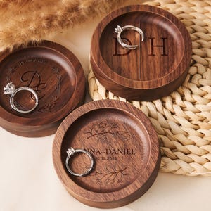 May include: Three wooden ring dishes with engraved designs. The first dish has the initials "D & H" engraved on it. The second dish has the initials "D" and a floral design engraved on it. The third dish has the text "Anna + Daniel 12.12.2023" and a floral design engraved on it.