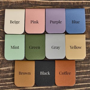 May include: A collection of eleven rectangular magnetic bookmarks with rounded bottom edges, each featuring a distinct color: beige, pink, purple, blue, mint, green, gray, yellow, brown, black, and coffee, with the color name printed on each.