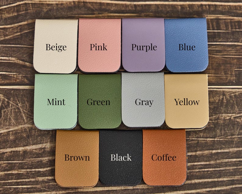 May include: A collection of eleven rectangular magnetic bookmarks with rounded bottom edges, each featuring a distinct color: beige, pink, purple, blue, mint, green, gray, yellow, brown, black, and coffee, with the color name printed on each.