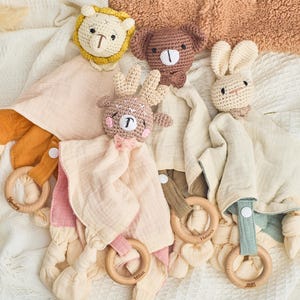 K&ouml;nnte beinhalten: Ein Set aus f&uuml;nf geh&auml;kelten Tierbabyspielzeugen mit Holzringen. Die Spielzeuge beinhalten einen L&ouml;wen, ein Reh, ein Kaninchen und zwei B&auml;ren. Die Spielzeuge sind alle beige und cremefarben.