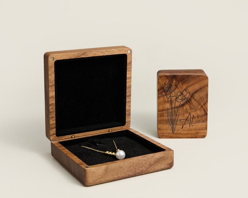 May include: A wooden box with a black velvet interior, a gold necklace with a pearl pendant, and a smaller wooden box with a floral design and the name "Alice" engraved on it.