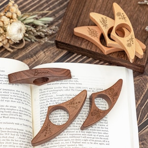 May include: Wooden thumb page holders in various shades of brown, some with floral engravings. One holder is engraved with the name "Bonnie". These accessories are designed to hold open a book.