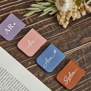May include: Four rectangular magnetic bookmarks in purple, dusty pink, blue, and brown. Each bookmark features white custom text: AR with a heart, Ava, Aria with a leaf sprig, and Sophia with a line accent. The bookmarks have a textured finish.