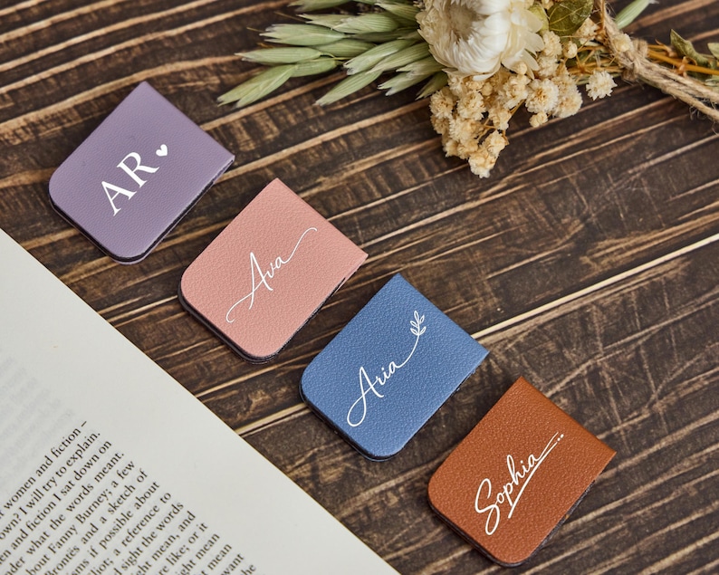 May include: Four rectangular magnetic bookmarks in purple, dusty pink, blue, and brown. Each bookmark features white custom text: AR with a heart, Ava, Aria with a leaf sprig, and Sophia with a line accent. The bookmarks have a textured finish.