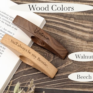 May include: Two wooden book page holders, one walnut and one beech, with engraved text. The walnut holder says "Victoria," and the beech holder says "You'll always be my Bestie." The image also shows the words "Wood Colors," "Walnut," and "Beech."
