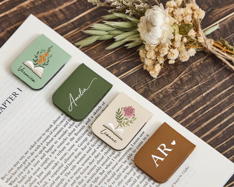 May include: Four rectangular magnetic bookmarks in sage green, olive green, cream, and brown. Each features custom text including the names Veronica, Amelia, Leanne, and the initials AR with a heart icon, plus floral and open book illustrations.