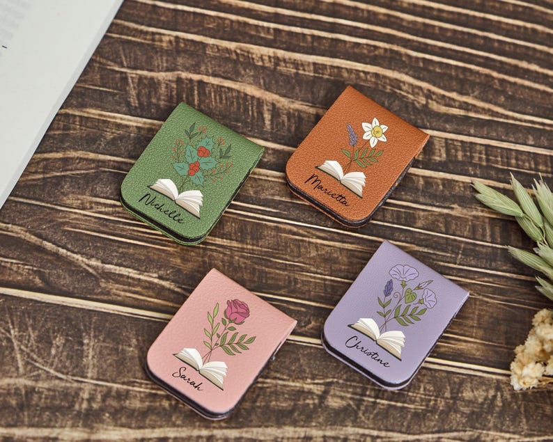 May include: Four rectangular magnetic bookmarks in green, tan, pink, and lavender. Each features an open book illustration with a different flower growing from the pages and a printed name: Nichelle, Marietta, Sarah, and Christine.