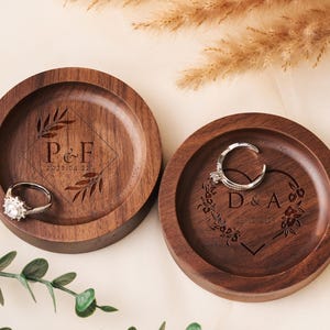 Op de afbeelding: Twee houten ringenschalen met gegraveerde initialen en data. De schaal links heeft de initialen "P&F" en de datum "2023.05.22". De schaal rechts heeft de initialen "D&A" en de datum "13.10.2023".