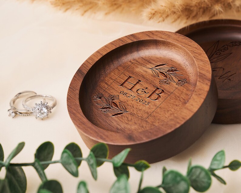 May include: A wooden ring dish with a floral design and the initials "H&B" engraved on it. The date "08-27-2023" is also engraved on the dish.
