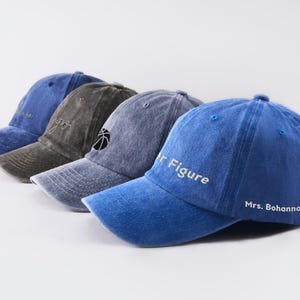 Op de afbeelding: Vier denim baseballpetten met verschillende geborduurde ontwerpen. De petten zijn in tinten blauw en grijs. De ontwerpen omvatten een basketbal, de woorden "Mr. Figure" en "Mrs. Bohannon".