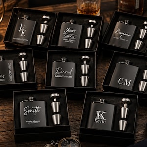 May include: Black flasks with personalised engravings, presented in black gift boxes. Each set includes a flask, a stopper, and two stainless steel shot glasses. The flasks are engraved with names, initials, and dates, ideal for groomsmen gifts.