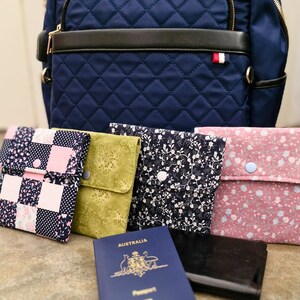 May include: Four small fabric pouches with different floral patterns, a blue passport with the word "Australia" on the cover, and a black passport holder. The pouches are arranged in a row on a brown surface.