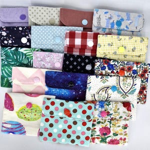 May include: A collection of 16 small fabric pouches with various patterns and colours. Each pouch has a button closure and is made of different fabrics, including floral, polka dot, geometric, and paisley.