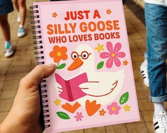 May include: A pink spiral-bound notebook with the text "JUST A SILLY GOOSE WHO LOVES BOOKS." The cover features a cartoon goose wearing glasses and reading a pink book, surrounded by colorful flowers.