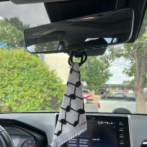 May include: A black and white checkered fabric hanging from the rearview mirror of a car. The fabric is a traditional Palestinian keffiyeh.