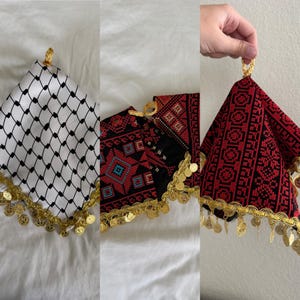 Peut inclure: Trois carrés de tissu à motifs différents avec une bordure de pièces d'or. Les carrés sont pliés en forme triangulaire. Les motifs des tissus sont noir et blanc, rouge et noir, et noir et rouge.