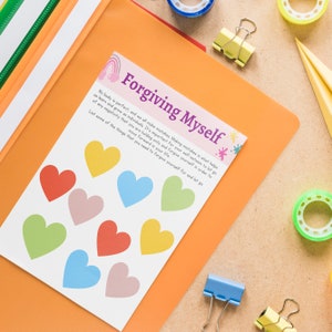 Op de afbeelding: Een witte kaart met de tekst "Forgiving Myself" in paars en regenboogkleurige harten. De kaart bevat een citaat over het vergeven van jezelf en het loslaten van negativiteit. De kaart ligt op een fel oranje oppervlak.