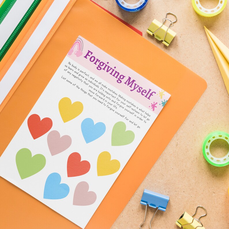 Op de afbeelding: Een witte kaart met de tekst "Forgiving Myself" in paars en regenboogkleurige harten. De kaart bevat een citaat over het vergeven van jezelf en het loslaten van negativiteit. De kaart ligt op een fel oranje oppervlak.