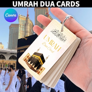 Könnte beinhalten: Ein Stapel Umrah Dua-Karten, gehalten in der Hand, mit einem silbernen Ring gebunden. Die Karten zeigen goldenen Text und eine Illustration der Kaaba. Der Hintergrund zeigt die Kaaba in Mekka und eine Menschenmenge.