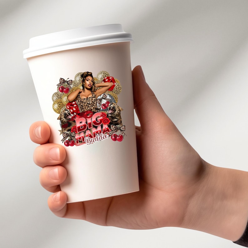 May include: A white paper coffee cup with a white lid. The cup features a graphic of a woman in a leopard print top, surrounded by gold balloons, red roses, and cherries. The text "BIG Mama Baddie" is displayed in red.