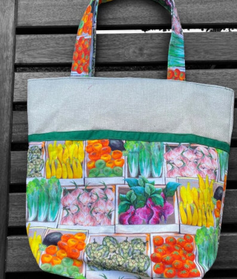 May include: A green and white canvas tote bag with a colourful print of various vegetables and fruits. The bag has a green fabric handle.