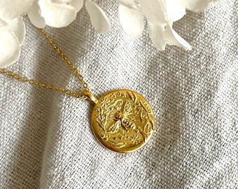 May include: A gold necklace with a round pendant featuring an embossed bee design surrounded by flowers and stars.