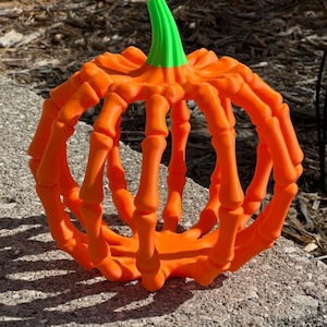 May include: A hollow, spherical pumpkin decoration constructed from orange, bone-shaped segments that form a cage-like structure. The top features a bright green, ribbed stem. The object has a matte finish and a rounded, symmetrical design.